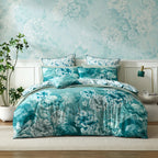 A soft blue teal and white floral bedding set styled on a bed in a bedroom with matching floral wallpaper, white wainscoting, a potted plant, and a bedside lamp.