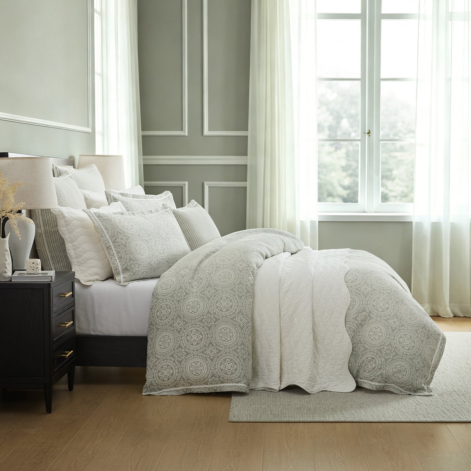 A light gray and white patterned bedding set styled on a bed in a bright, modern bedroom with gray paneled walls, white curtains, and a wooden floor.