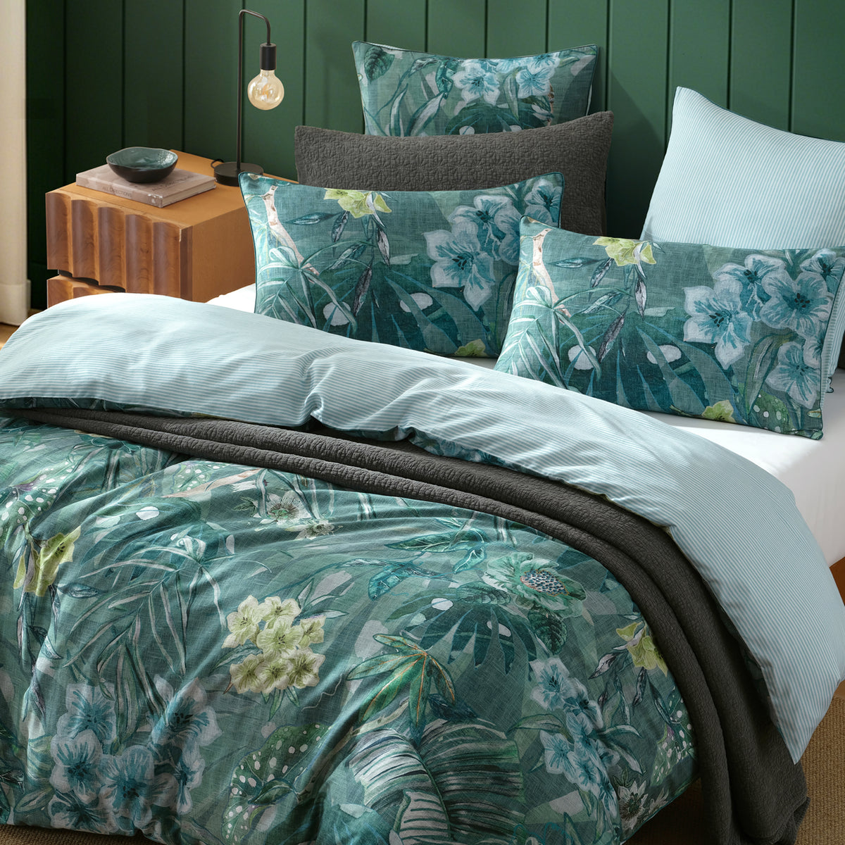 Logan & Mason Lila Surf Duvet Cover Set in Green styled with matching tropical floral pillowcases, a charcoal quilted throw and a contrasting pale blue striped reverse.