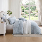 Private Collection Garden Veil 100% Cotton Jacquard Duvet Cover Set in Chambray featuring a delicate white floral design, styled with matching pillowcases and white quilted bedding in a bright bedroom.
