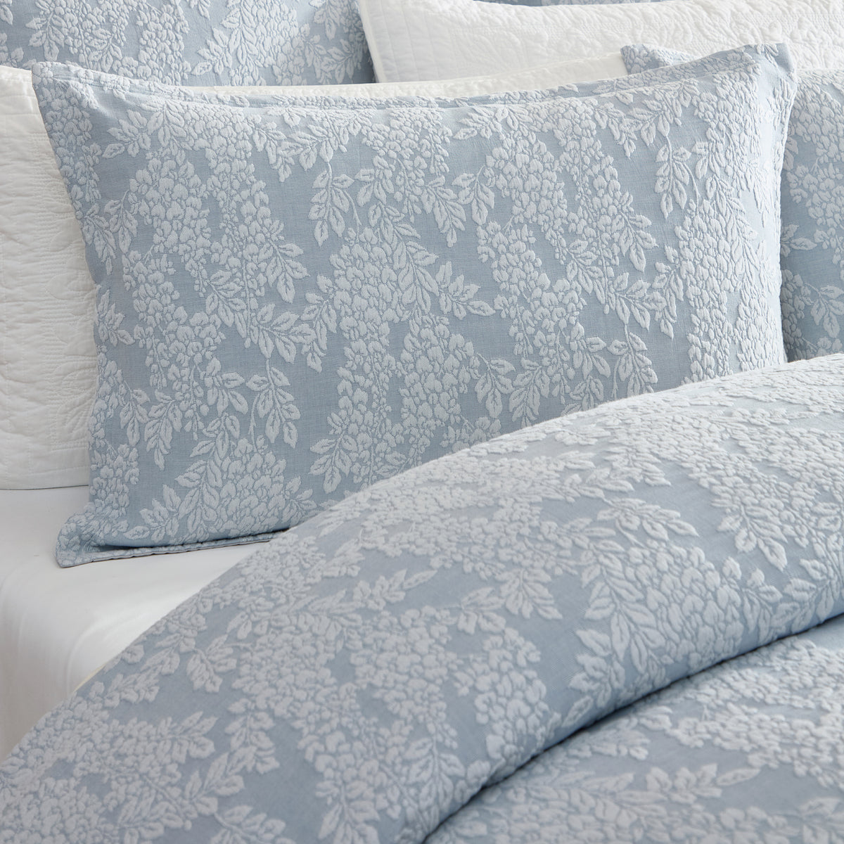 Close-up of the Private Collection Garden Veil Duvet Cover Set in Chambray, showcasing the textured white floral jacquard pattern on soft blue fabric.