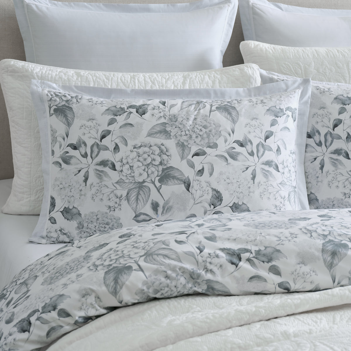 Close-up of the Private Collection Hydrangea Duvet Cover Set with matching floral pillowcases, soft grey striped European pillowcases and layered white bedding.