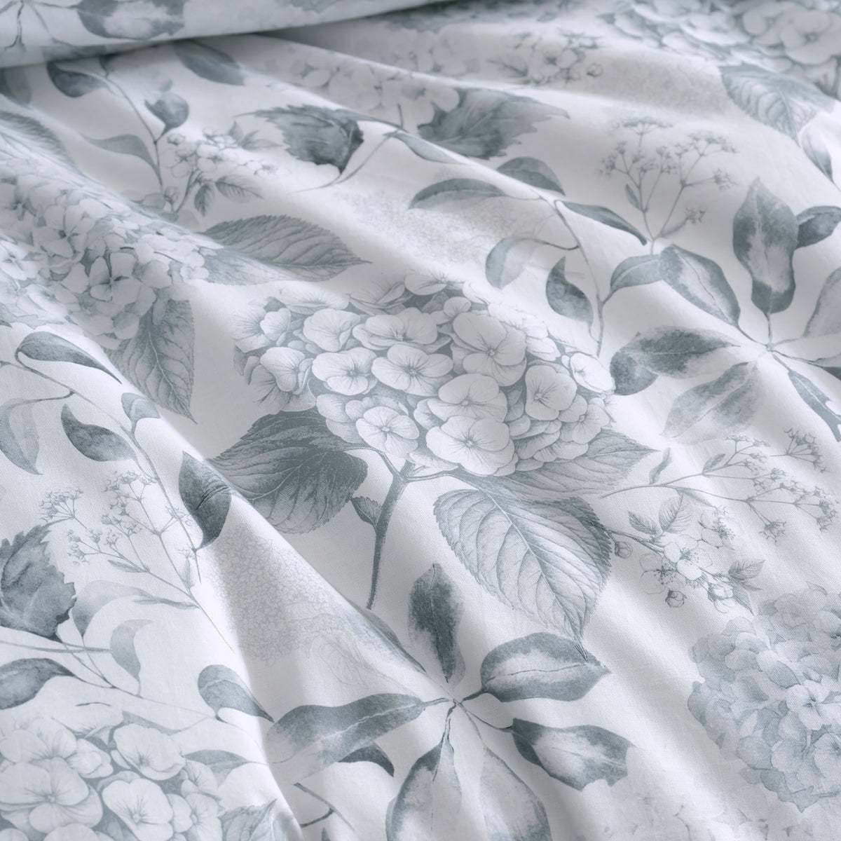 Close-up of the Private Collection Hydrangea Duvet Cover Set, showcasing the delicate grey hydrangea flowers and leafy botanical pattern on a white background.