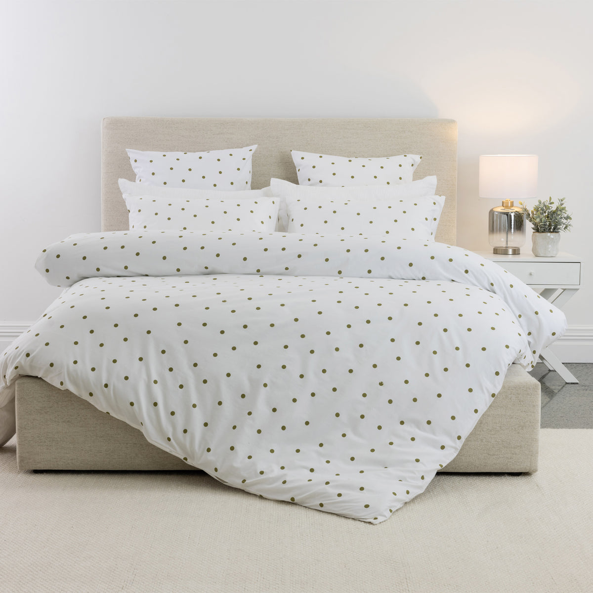 Pure & Simple Monroe Cotton Duvet Cover Set in white with olive polka dots, styled on a bed with coordinating pillowcases against a neutral upholstered headboard.