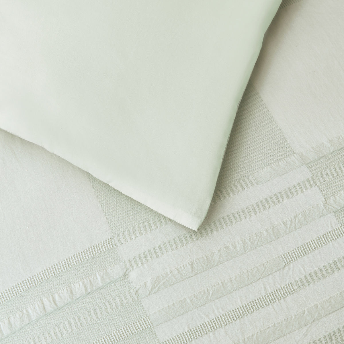 Close-up of the Baker St. Linen Zane Duvet Cover Set in Sage, showing the smooth reverse fabric alongside the textured jacquard front.