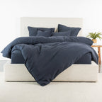 A midnight hue bedding set with a duvet cover and matching pillows styled on a bed with a light beige upholstered frame, set against a clean white background.