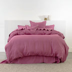 A bed dressed in a berry bedding set with matching pillows and a ruffled duvet cover, set against a white paneled headboard and light gray carpet.