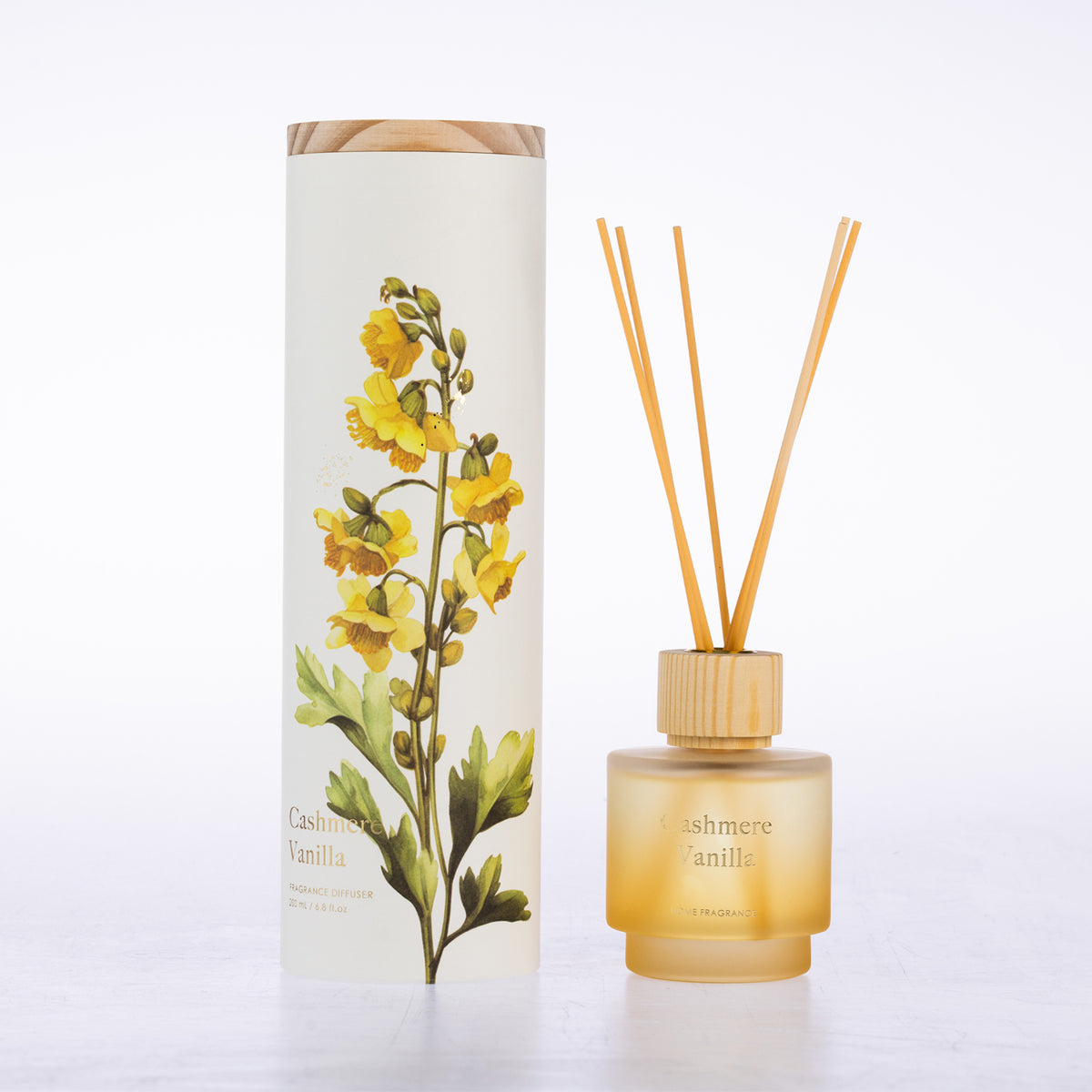 A frosted glass with reeds diffuser beside its matching cylindrical box packaging.