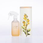A frosted glass room spray beside its matching cylindrical box packaging.