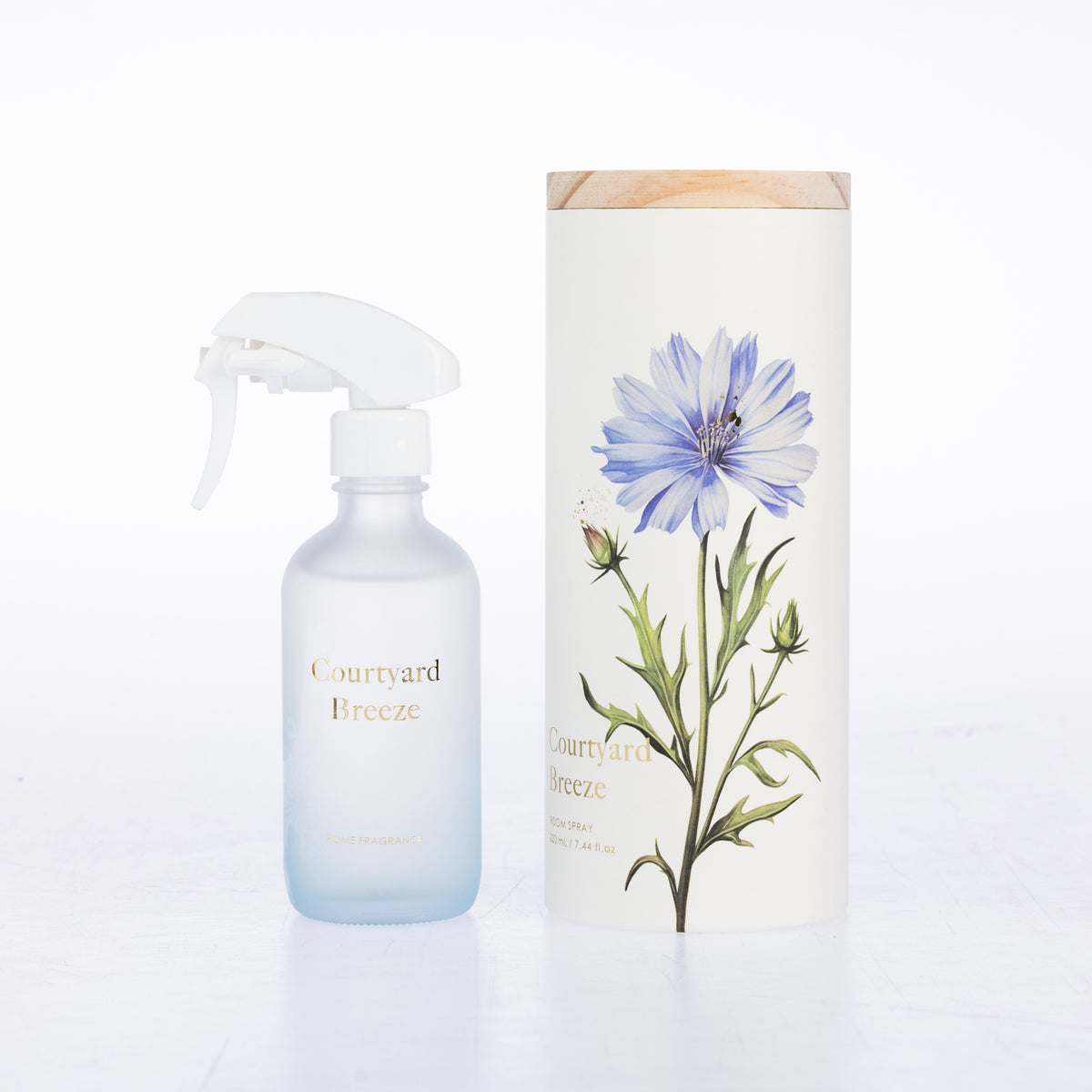 A frosted glass room spray beside its matching cylindrical box packaging.