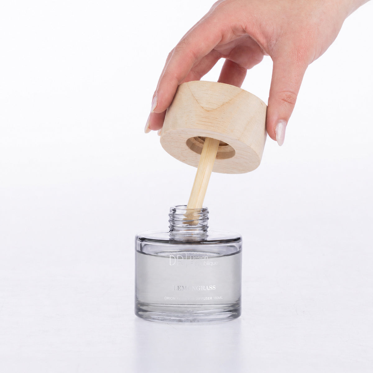Design Republique Lemongrass Orion Reedless Diffuser shown open with the natural wood-look lid and bamboo diffuser insert being lifted from the clear glass vessel.