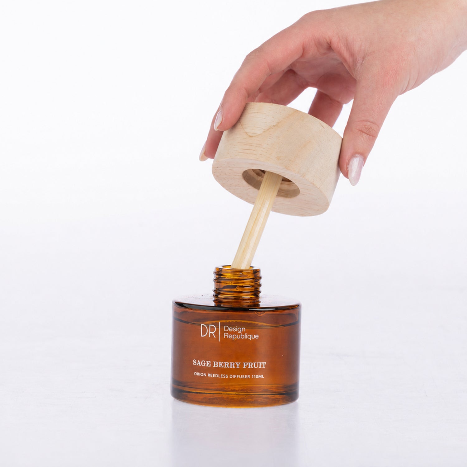 Design Republique Sage Berry Fruit Orion Reedless Diffuser shown open with the natural wood-look lid and bamboo diffuser insert being lifted from the amber glass vessel.