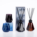 Design Plus Home fragrance range featuring faceted glass reed diffusers and coordinating scented candles in blue, purple, smoky black and amber tones.