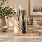 A styled home fragrance range on a stone tray featuring reed diffusers and glass jar candles.