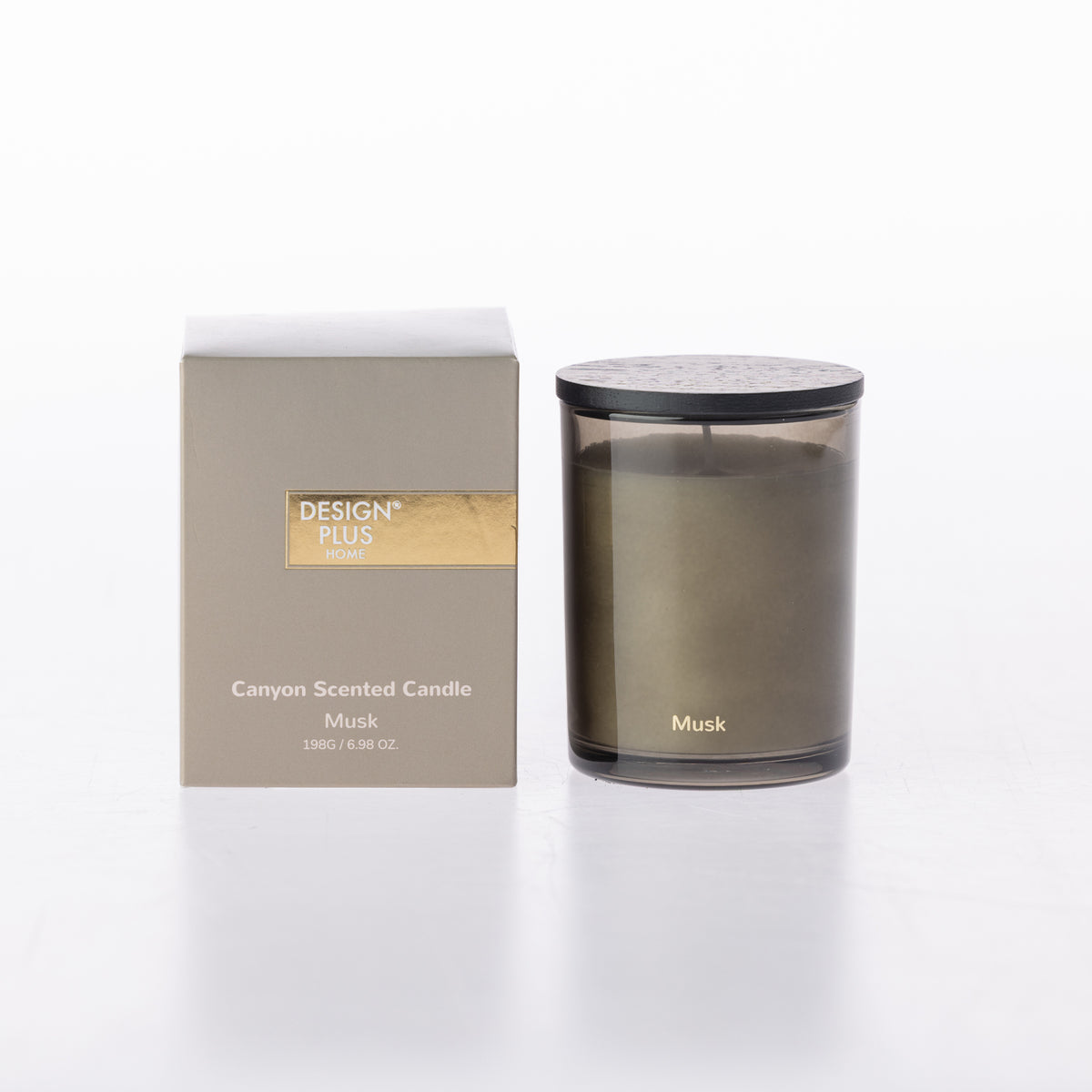 A Design Plus Musk Canyon Scented Candle in a smoky glass jar with a black lid, shown next to its packaging box with gold foil detailing on a white background.