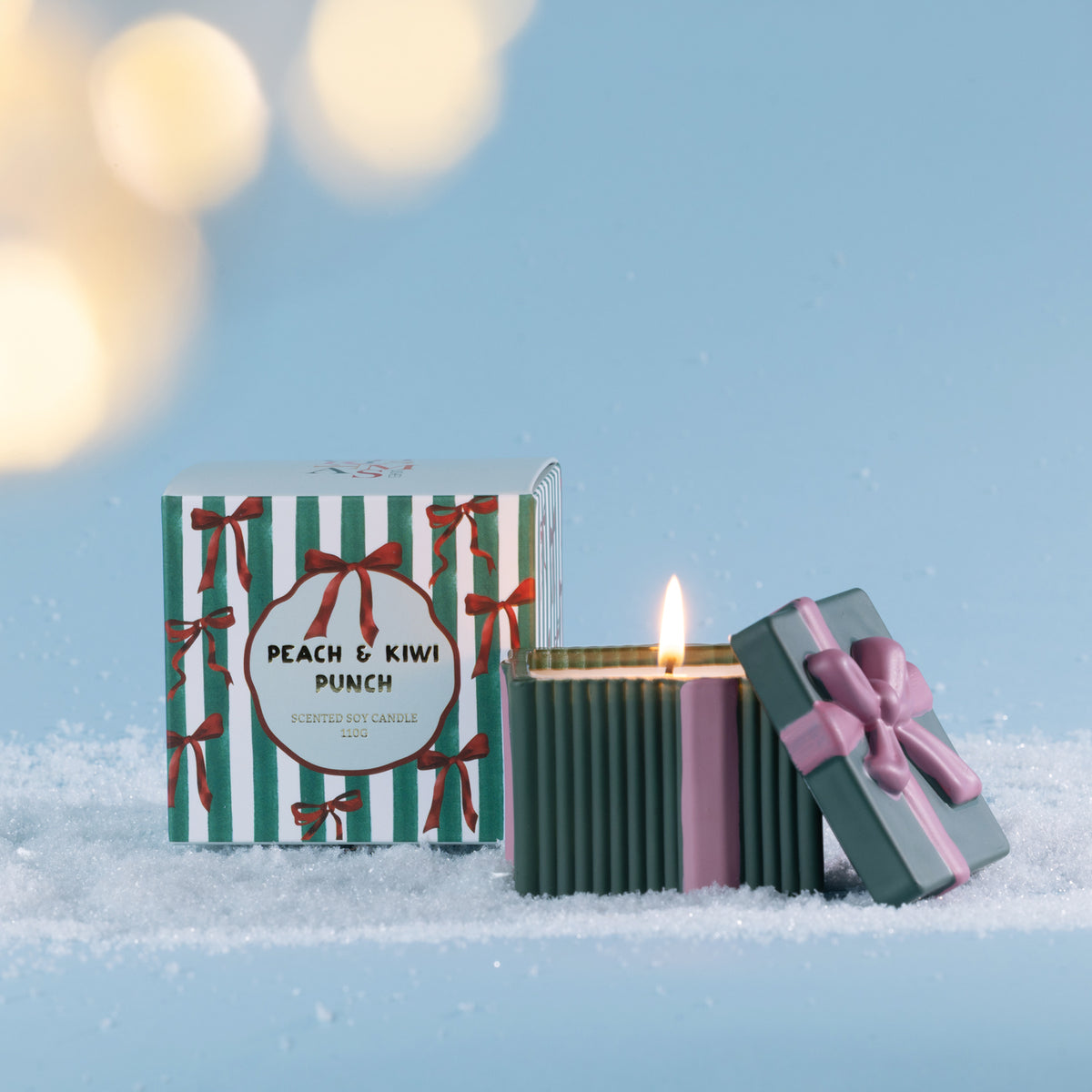 Christmas Wishes Bow Candle in a Box 110g Peach & Kiwi Punch – Green ribbed scented soy candle with pink ribbon detailing and a bow-topped lid, displayed beside its coordinating green and white striped Peach & Kiwi Punch gift box.