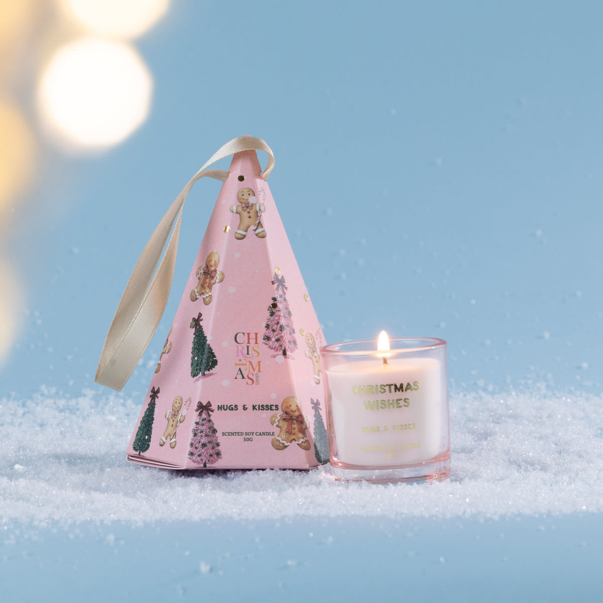 Christmas Wishes Mini Candle in Gift Box 50g Hugs & Kisses – Hugs & Kisses scented soy candle in a clear glass vessel, displayed beside its pink cone-shaped Christmas gift box decorated with gingerbread characters and festive trees.