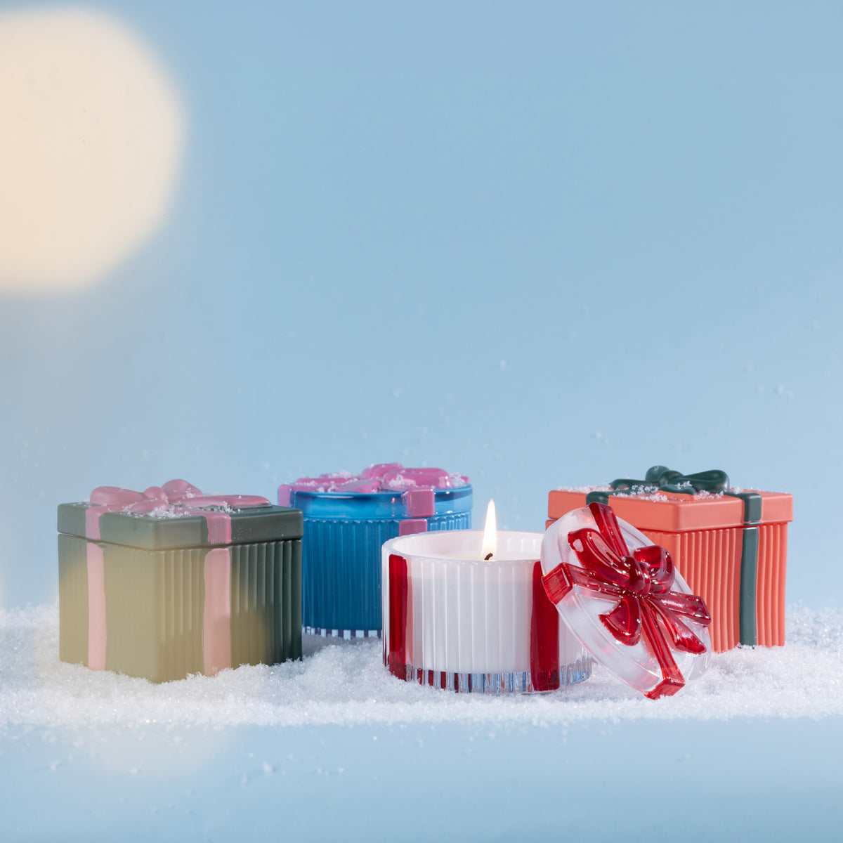Christmas Wishes Bow Candle in a Box 110g Range – Festive collection of gift-style scented candles displayed in decorative ribbed vessels with bow-topped lids in assorted colours, styled together amongst faux snow.