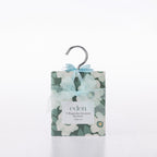 Eden Magnolia Scented Closet Sachets 4 Pack featuring dark green packaging with white magnolia flowers, a pale blue ribbon bow and a silver hanging hook.