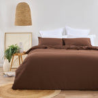 Design Plus August Cotton Waffle Duvet Cover Set in Brick styled in a contemporary bedroom with matching waffle weave pillowcases, white layered pillows, natural timber furniture, woven lighting, and botanical décor.