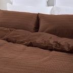 Design Plus August Cotton Waffle Duvet Cover Set in Brick styled on a bed, highlighting the textured waffle weave duvet cover, matching pillowcases, and smooth reverse fabric.