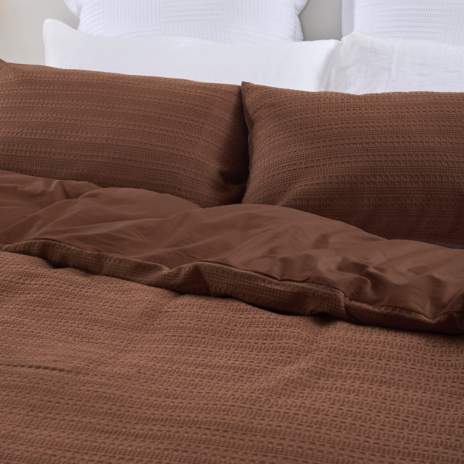 Design Plus August Cotton Waffle Duvet Cover Set in Brick styled on a bed, highlighting the textured waffle weave duvet cover, matching pillowcases, and smooth reverse fabric.