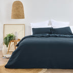 Design Plus August Cotton Waffle Duvet Cover Set in Diesel Blue styled in a contemporary bedroom with matching waffle weave pillowcases, white layered pillows, natural timber furniture, woven lighting, and botanical décor.