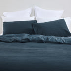 Design Plus August Cotton Waffle Duvet Cover Set in Diesel Blue styled on a bed, highlighting the textured waffle weave duvet cover, matching pillowcases, and smooth reverse fabric.
