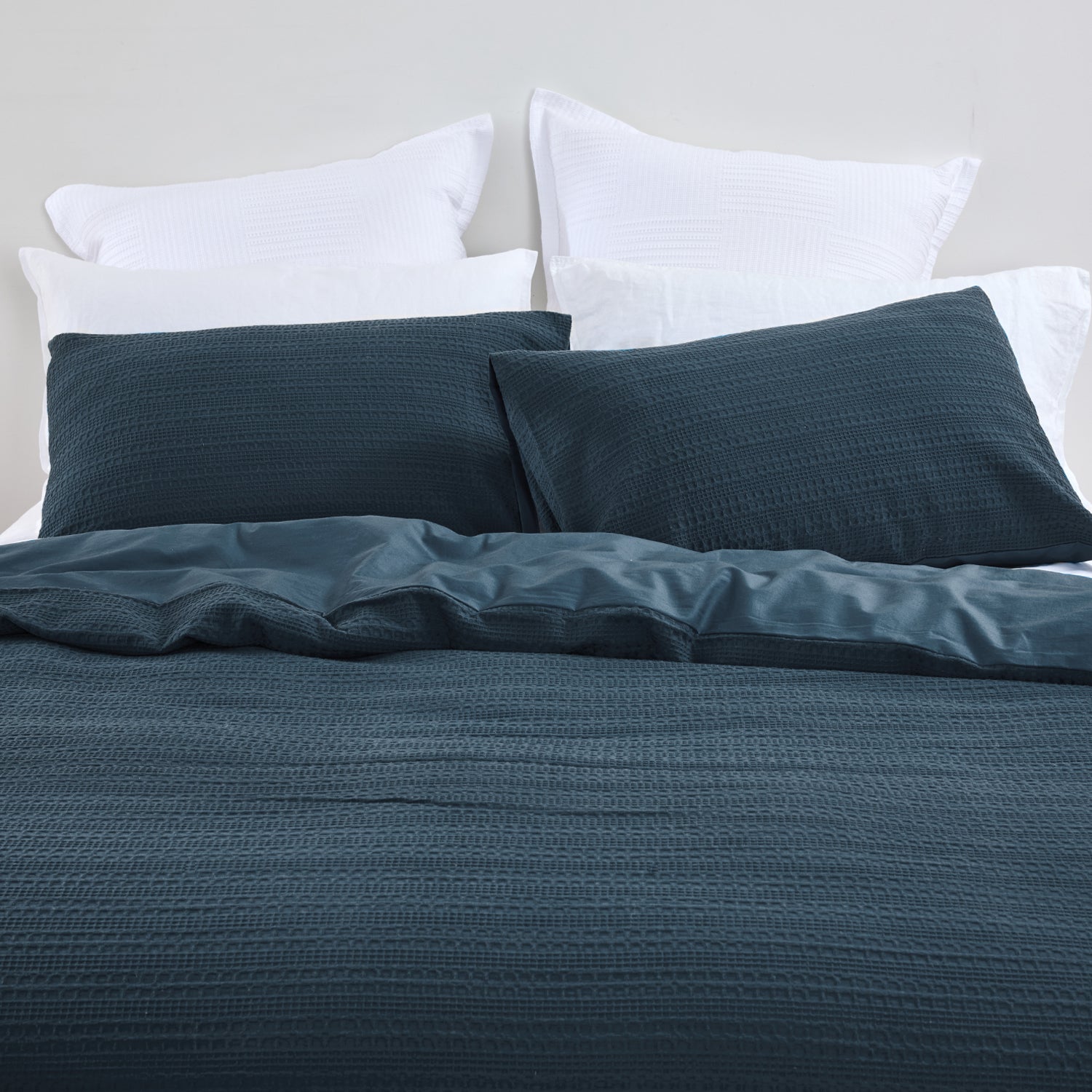 Design Plus August Cotton Waffle Duvet Cover Set in Diesel Blue styled on a bed, highlighting the textured waffle weave duvet cover, matching pillowcases, and smooth reverse fabric.