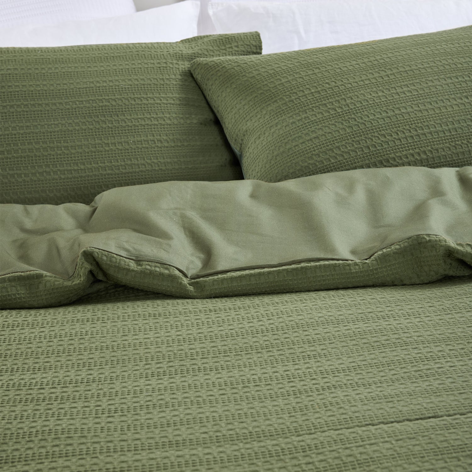 Design Plus August Cotton Waffle Duvet Cover Set in Green styled on a bed, highlighting the textured waffle weave duvet cover, matching pillowcases, and smooth reverse fabric.