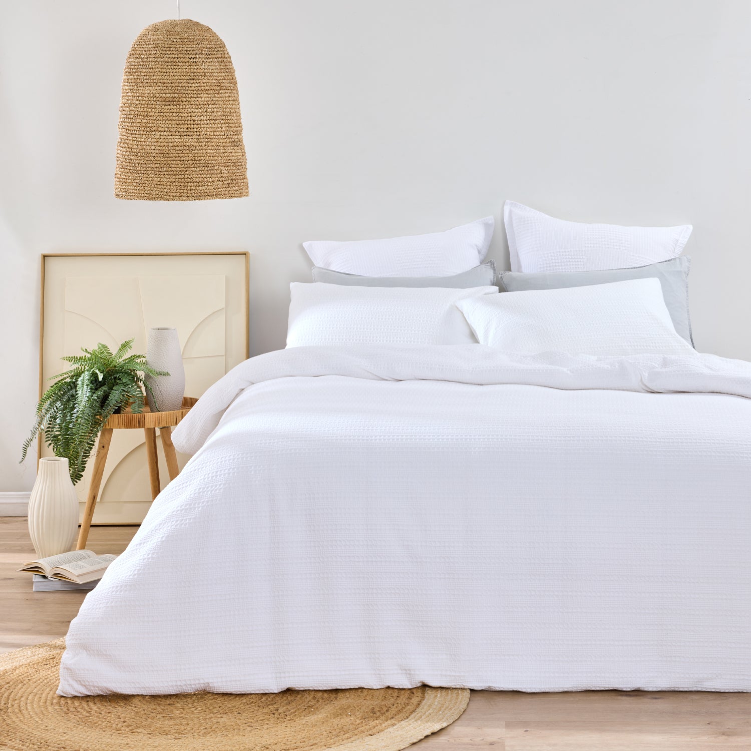 Design Plus August Cotton Waffle Duvet Cover Set in White styled in a contemporary bedroom with matching waffle weave pillowcases, white layered pillows, natural timber furniture, woven lighting, and botanical décor.