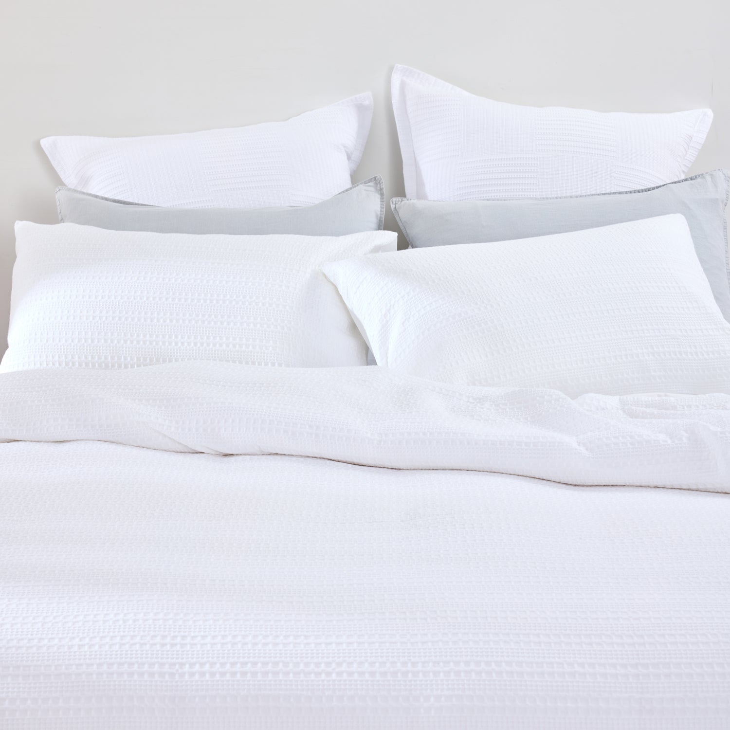 Design Plus August Cotton Waffle Duvet Cover Set in White styled on a bed, highlighting the textured waffle weave duvet cover, matching pillowcases, and smooth reverse fabric.