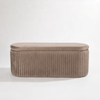 Taupe pleated velvet storage bench with a rounded rectangular silhouette and vertical channel detailing, shown front-on against a white background.