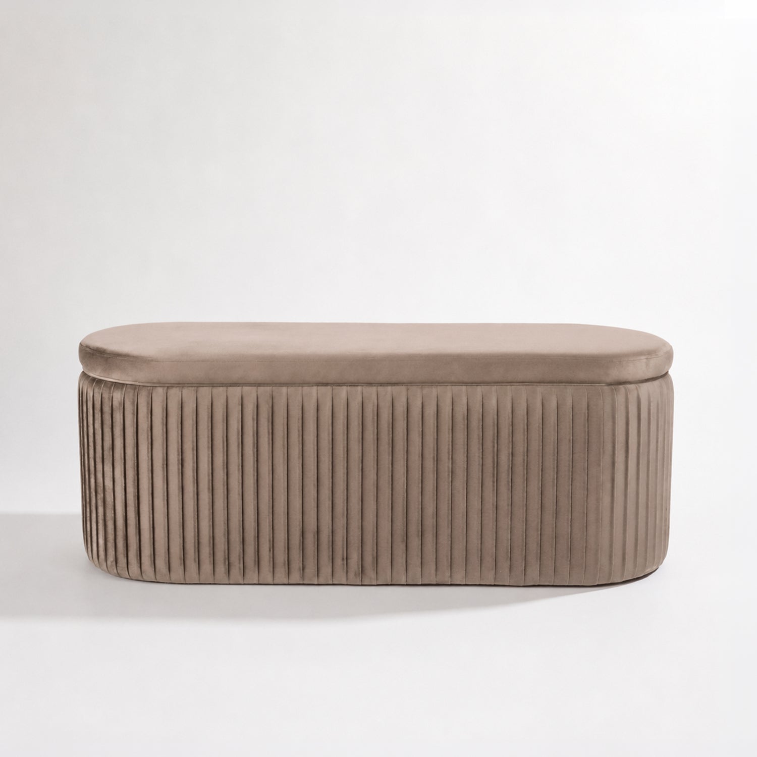 Taupe pleated velvet storage bench with a rounded rectangular silhouette and vertical channel detailing, shown front-on against a white background.