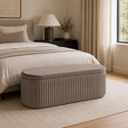 Taupe pleated velvet storage bench with vertical channel detailing placed at the foot of a bed in a warm, neutral-toned bedroom.