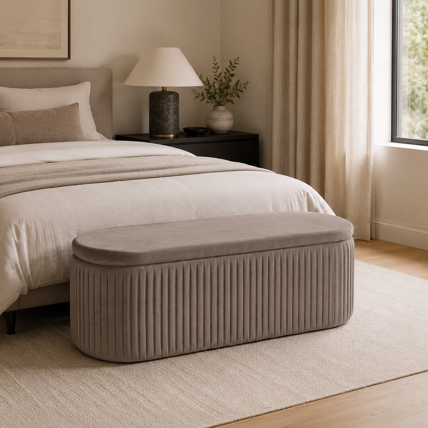 Taupe pleated velvet storage bench with vertical channel detailing placed at the foot of a bed in a warm, neutral-toned bedroom.