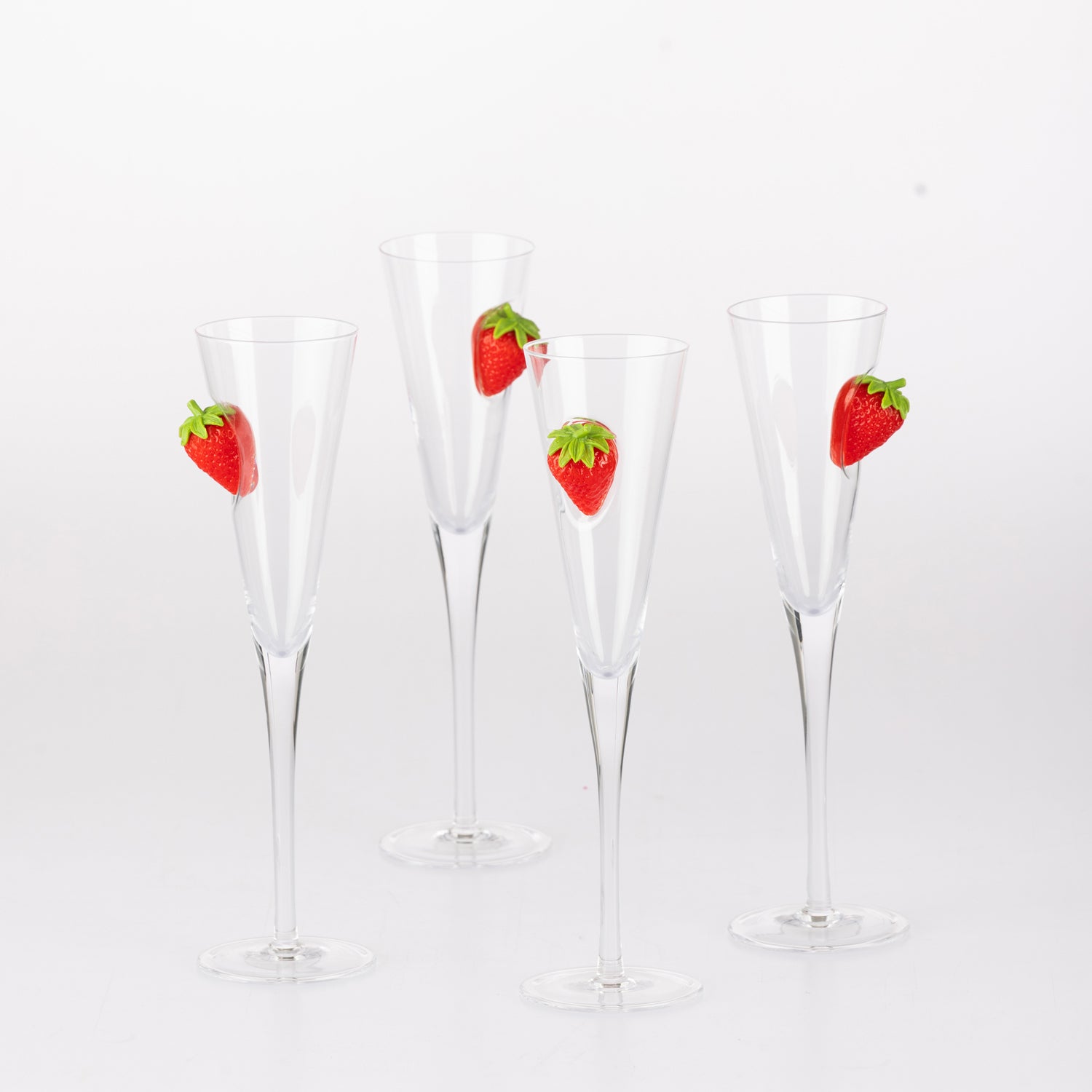 Four clear champagne flutes with raised strawberry embellishments arranged together against a white background.