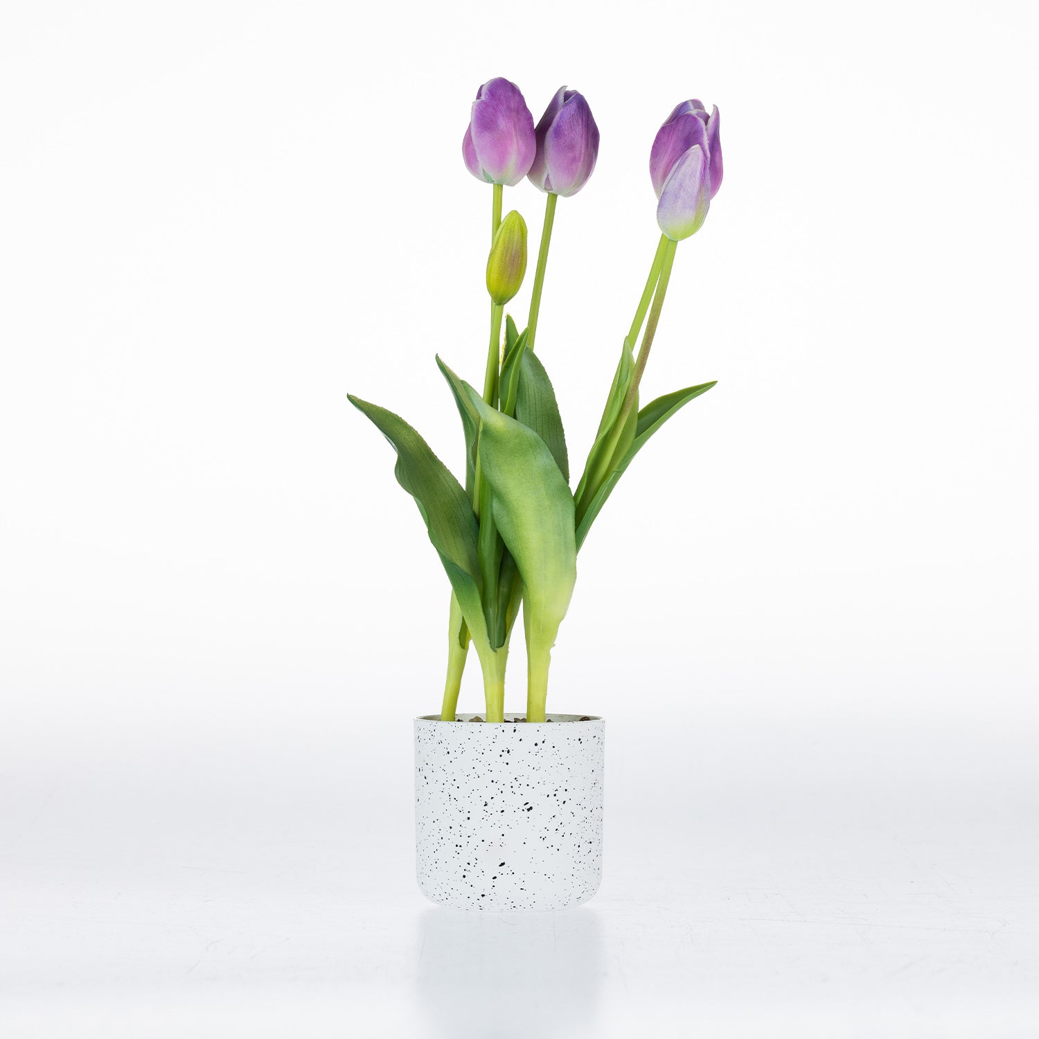 Artificial lilac tulip arrangement with realistic blooms and green foliage displayed in a white speckled pot.