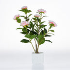 Artificial pink camellia plant with green foliage in a white speckled ceramic pot.