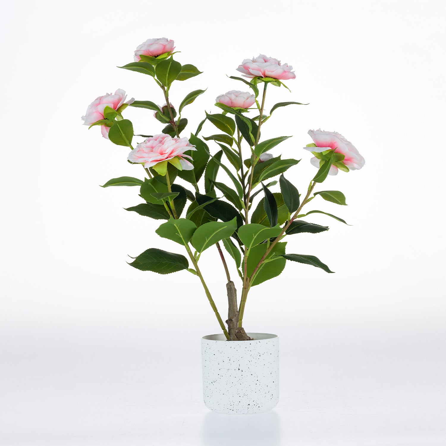 Artificial pink camellia plant with green foliage in a white speckled ceramic pot.