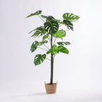 Artificial monstera plant with split green leaves displayed in a woven basket.