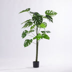 Artificial monstera plant with split green leaves in a black nursery pot.