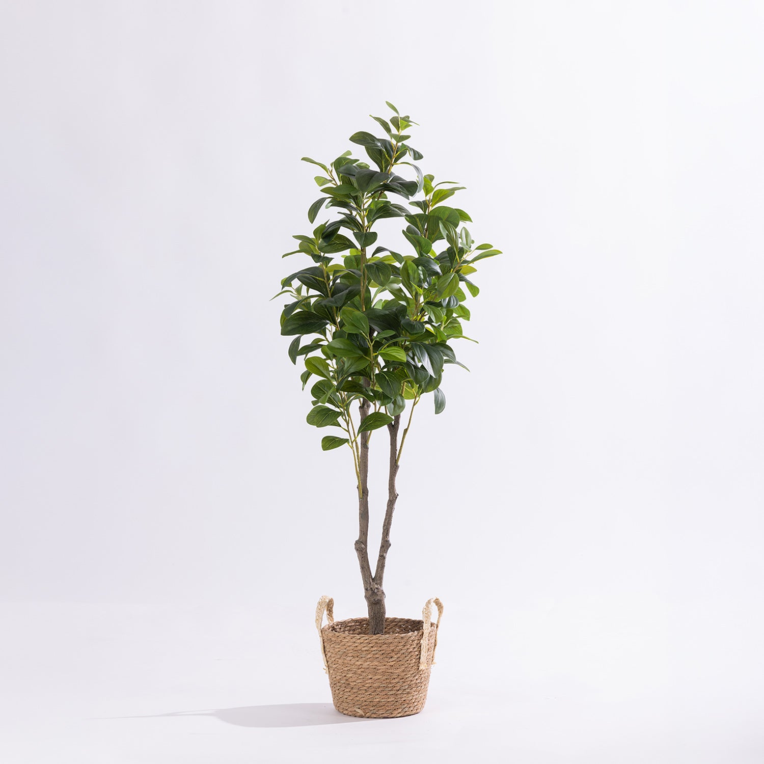 Artificial radiator tree with glossy green foliage displayed in a woven basket against a white background.