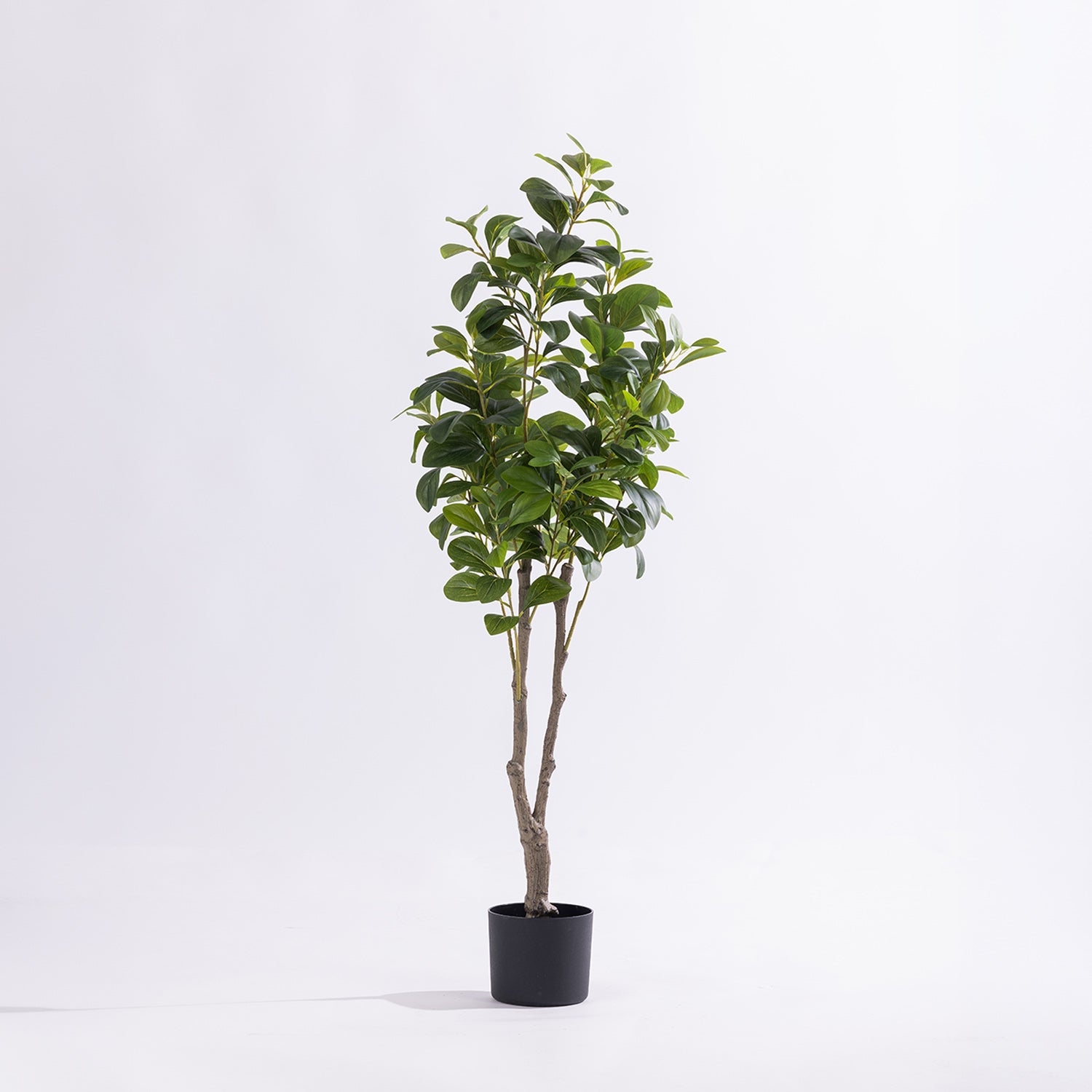 Artificial radiator tree with lush green foliage in a black nursery pot against a white background.