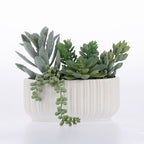 A faux succulent arrangement in a white ribbed ceramic pot, photographed on a clean white background.