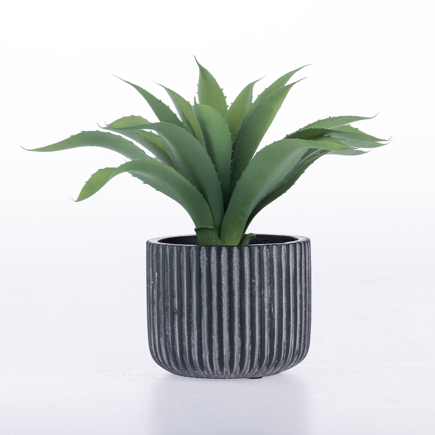 An artificial green succulent plant with spiky leaves in a dark gray ribbed cylindrical pot, set against a plain white background.