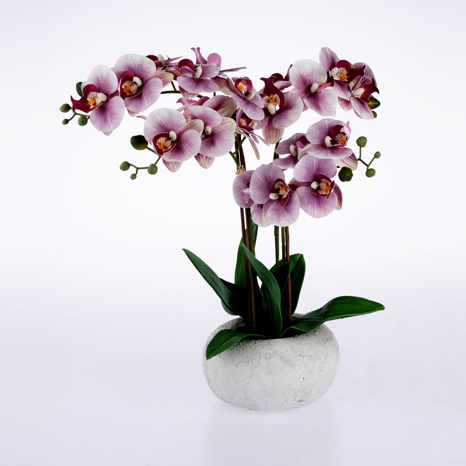 A potted artificial orchid arrangement with pale pink to purple blossoms, dark green leaves, and a round textured white pot on a clean white background.