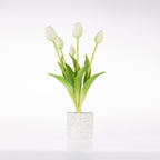 A small artificial tulip arrangement with five white tulip buds and green leaves in a speckled white cylindrical pot, photographed on a clean white background.
