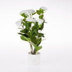 An artificial white flower arrangement with green leaves in a speckled white cylindrical pot, photographed on a seamless white background.