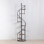 Empty black spiral display shelf with wood-look shelves, shown against a white wall on a cream carpet.
